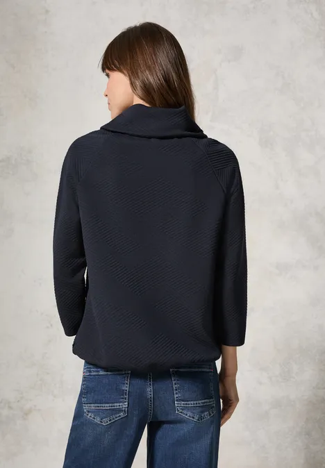Frau mit dunkelblauem Pullover und Jeans, Rückenansicht.